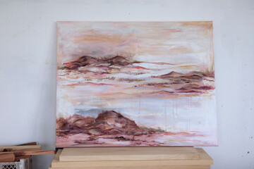 Art studio. View of romantic painting depicting the ocean, waves and rocks in the beach at sunset. Beautiful brushstrokes and dusk palette of pink, magenta, orange and red colors.