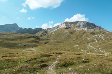 A narrow pathway along a high plateau in Italian Dolomites. Stony landscape, with a bit of green grass. High mountain chains in the back. Desolated and remote landscape. Natural habitat. A few clouds