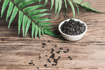 Spa - composition with. Black Sea salt for body scrubbing on a wooden table. Green leaves in the background, blur, copy space.