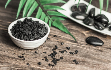 Spa - composition with stones and black sea salt on a wooden table. Blurred green background with a green twig. Copy space