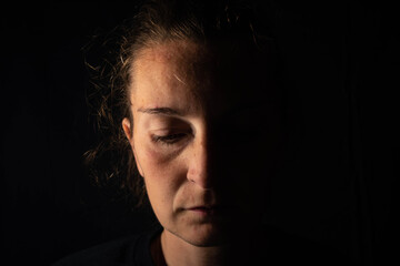 Dark portrait of a serious woman with half illuminated face. The woman is looking down showing sadness or depression