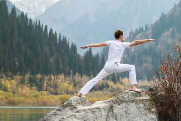 A man practices yoga on a background of mountains. Pose Virabhadrasana 2 or warrior.