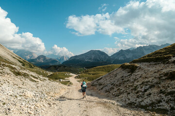 Fototapeta premium A woman hiking along a high plateau in Italian Dolomites. High mountains around. The area is partially overgrown with grass and partially covered with stones. Remote and desolate area. Freedom