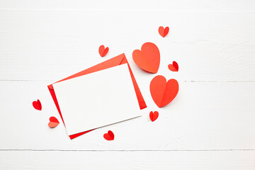 Greeting card mockup, white blank card with paper envelope and red parer hearts on wooden table background