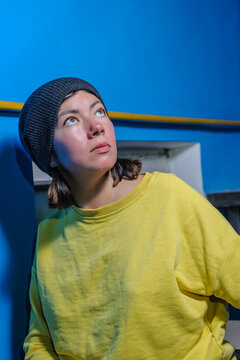 young woman in knit cap and yellow sweater looking up on blue background