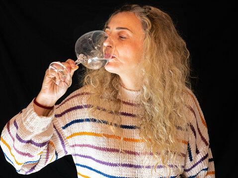 A portrait of a beautiful blonde female drinking white wine on the black background