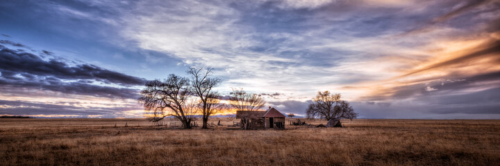 An old farmhouse on the eastern plains of Colorado in a rural setting at sunset. The sky is...