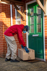 Hampshire, England, UK. 2020, Male courier delivering parcels and packages during Covid-19 epidemic wearing gloves and a mask.