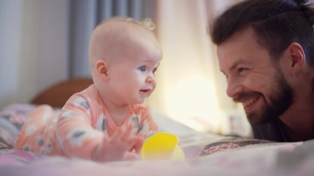 Smiling dad and his little daughter have fun together in the bedroom.