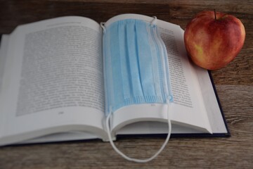 Maseczka ochronna w otwartej książce obok czerwone jabłko