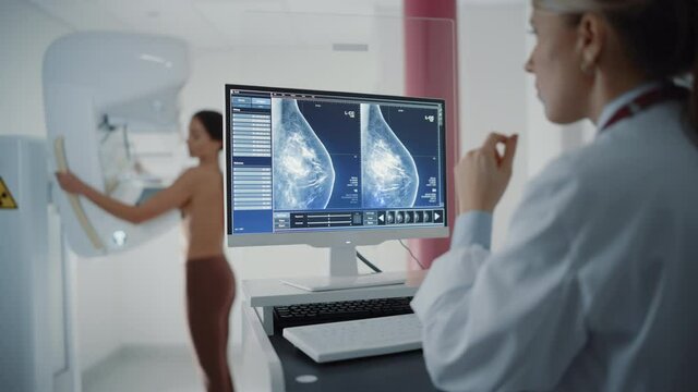 Computer Screen in Hospital Radiology Room: Beautiful Multiethnic Adult Woman Standing Topless Undergoing Mammography Screening Procedure. Screen Showing the Mammogram Scans of Dense Breast Tissues.