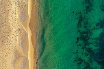 Sea coastline, above view, beach background. Ocean surface seashore, seaweed on the water. Footprints on the sand.