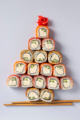 Edible christmas tree made from sushi with salmon, tuna and eel with philadelphia cheese, pickled ginger and sticks for sushi on white. Vertical format. Top view