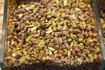 Peeled pistachios in a transparent plastic container on a store counter.