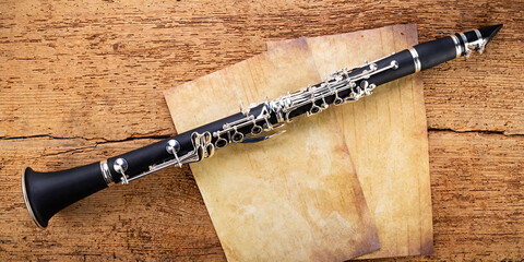 black wooden clarinet  silver woodwind musical brass instrument with old empty vintage music sheet copy space paper on retro oak wood background. classic orchestra symphony background.