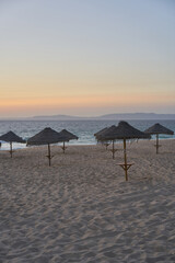 Empty beach at sunset in Comporta, Portugal with straw summer umbrellas