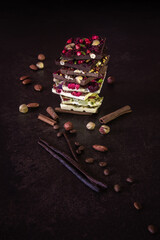 A stack of beautiful hand-made dark and white chocolate bars containing nuts and berries on a dark...