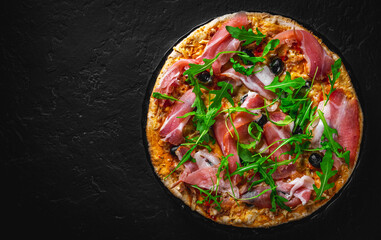 Pizza with Mozzarella cheese, ham, pepper, olive, meat, Tomato sauce, Spices and Fresh arugula. Italian pizza on black plate on Dark grey black slate background