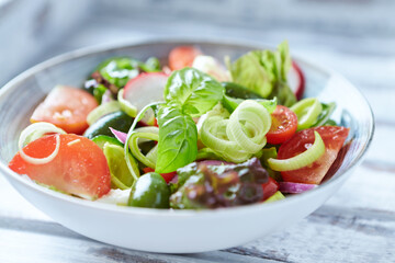 Salad with feta cheese, radish, rocket, green olives, tomatoes, cucumber and fresh basil. Bright wooden background. Close up. 