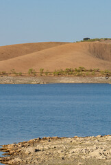 Desert like hill landscape with reflection on the water on a dam lake reservoir with blue sky in Terena, Portugal