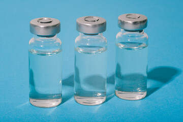 Coronavirus vaccine. Glass bottle with liquid on a blue background. Vaccination against covid-19. Treatment of diseases, infections and viruses. Pharmaceuticals and healthcare