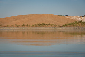 Fototapeta na wymiar Desert like hill landscape with reflection on the water on a dam lake reservoir with blue sky in Terena, Portugal