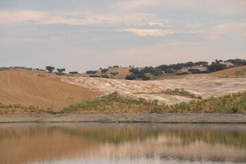 Fototapeta premium Desert like hill landscape with reflection on the water on a dam lake reservoir at sunset in Terena, Portugal