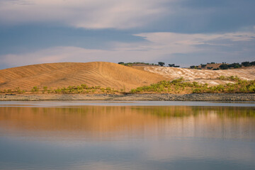 Desert like hill landscape with reflection on the water on a dam lake reservoir at sunset in Terena, Portugal