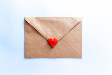 love letter in a craft envelope with clay red heart on light blue background.