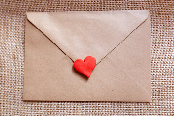 love letter in a craft envelope with clay red heart on a jute background.