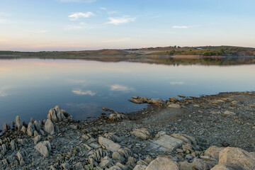 Lucefecit Dam in Terena with reflection on the lake reservoir and rocks on the foreground, in Portugal