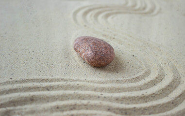 brown Zen stone on beige sand with abstract wave patterns. The concept of harmony, balance and meditation, spa, relaxation.