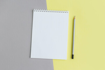 Notebook with blank page and pencil on a yellow and grey background.