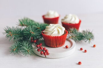 Tasty cupcakes decorated with spruce branches and red berries on a white wooden background. Sweets for the celebration Christmas.