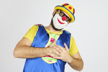 A clown in a bright blue and yellow suit and mask holds his heart with his hands, got sick