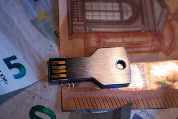 USB flash drive in the form of a key on the table, the background of blurred euro banknotes
