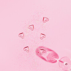 Chrystal champagne glass with heart shaped confetti on pastel pink background. Minimal style.