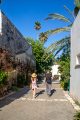 Fototapeta na wymiar Young woman and man walking down the street by the wall of hanging plant pots with flowers and irrigation systemat the Midrechov Street in Zichron Yaakov Israel