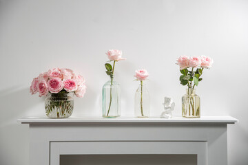 Bouquet of pink roses in a glass figured vase on a white fireplace console. A faience figurine of...