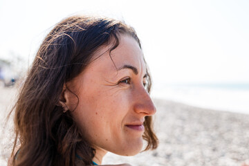 A smiling woman is standing on the seashore.