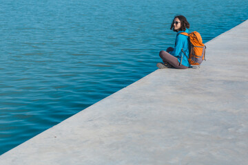 A woman with a backpack sits on the river bank