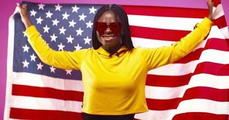 Happy patriotic African American holding US flag while standing isolated over pink background