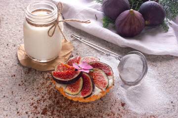 fig tart and a glass of milk on the stone textured backdrop. Concept photo with powdered sugar, sifter, crumbles and whole fig and tree branches on white table cloth. natural daylight. 
