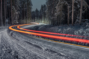 Forest road in winter with car light trails - obrazy, fototapety, plakaty
