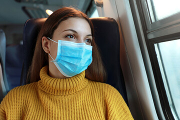 Fototapeta na wymiar Close up of female commuter with surgical face mask looking through train window. Train passenger with protective mask travels sitting in business class looking through the window.