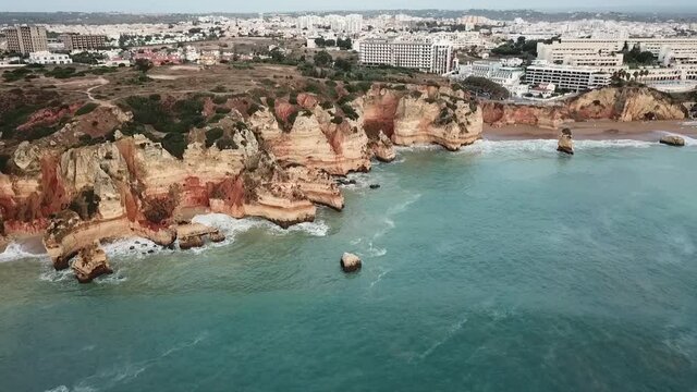 Lagos Portugal Atlantic ocean drone shot aerial view look over blue water waves sunrise morning limestone coastline sea pillars hidden grottos Praia de Dona Ana flying towards the beach