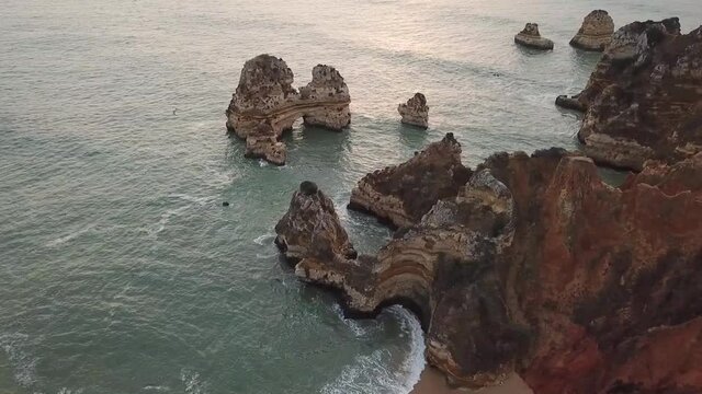 Lagos Portugal Atlantic ocean drone shot aerial view look over the rocks blue water waves sunrise morning limestone coastline sea pillars hidden grottos Praia do Camilo pan to right and fly towards