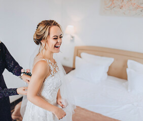 Morning of the bride. The girlfriend fastens a corset to the blonde bride. Wedding interior. Emotions of the bride.