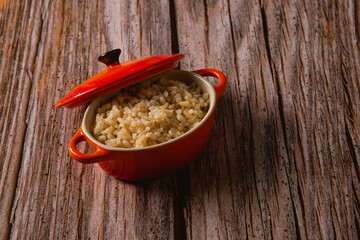 A small red pan with rice, on top of a wooden surface small red pan with rice, on top of a wooden surface