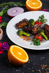 Grilled pork ribs in honey glaze with tomatoes and broccoli on a dark background